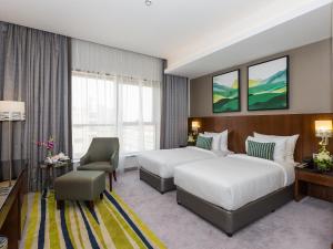a hotel room with two beds and a chair at Flora Al Barsha Hotel At The Mall in Dubai