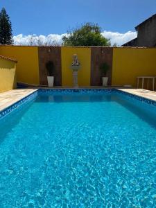 a swimming pool with blue water in front of a yellow building at Pousada na Praia Maricá in Maricá