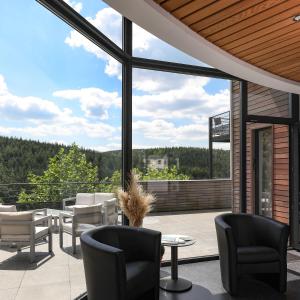 eine Terrasse mit Stühlen, Tischen und großen Fenstern in der Unterkunft Hotel Bô Rivage -- Eden-Ardenne in Neufchâteau