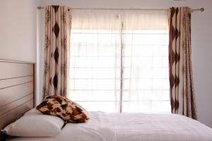 a bed with a pillow sitting next to a window at JRK Apartments & Services Limited in Lusaka