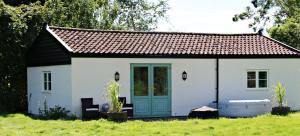 un piccolo cottage bianco con una porta blu di The Lodge - 2 acres of garden with hot tub and fire pit and BBQ a East Harling