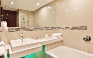 een badkamer met een wastafel, een spiegel en een bad bij Holiday Inn Johannesburg-Rosebank, an IHG Hotel in Johannesburg