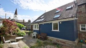 a blue house with a patio and a church at Fire Station Cottage in Comrie