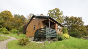 a wooden barn with a porch on a grass field at Morenish Mews Killin Cottage in Morenish