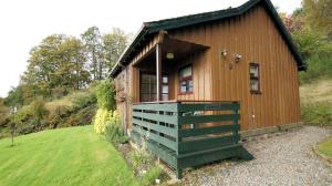 een kleine houten hut met een groene veranda in een veld bij Morenish Mews Kenmore Cottage in Morenish