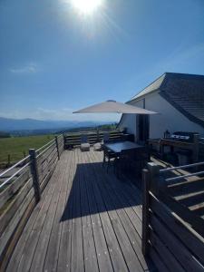 une terrasse en bois avec une table et un parasol dans l'établissement Maison entourée d animaux en pleine campagne, à Lasseube