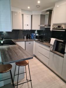 una cocina con armarios blancos, mesa y taburetes en 2 bed Home From Home Apartments, en Londres