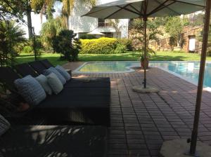 a couch sitting under an umbrella next to a pool at Plumbago Guest House in Hazyview