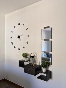 une horloge sur un mur blanc avec deux plantes dans l'établissement 270°, à Hydra