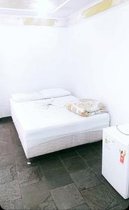 Una cama blanca sentada en una habitación junto a una nevera. en Hotel Estação Norte - Fácil acesso ao Imbel e o distrito industrial e colégio Militar - By Up Hotel, en Juiz de Fora