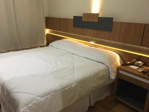 a bed in a hotel room with a phone on a table at Hotel Aero Park e Estacionamento in Londrina