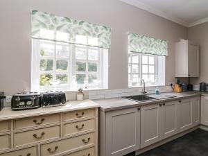 una cocina con armarios blancos, fregadero y ventanas en Clarence House en Dalton in Furness