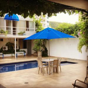 a table with chairs and a blue umbrella next to a pool at Hotel Casa Victoria Rodadero Reservado in Gaira