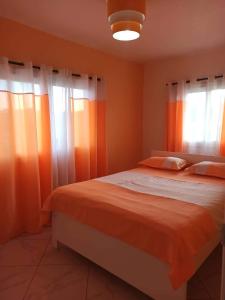 a bedroom with a bed with orange sheets and windows at Appartements Andrian Location in Antananarivo