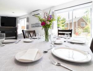 una mesa de comedor con platos blancos y un jarrón de flores en Détente Orford 111 condo/chalet en Orford