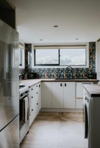 a kitchen with white cabinets and a large window at Kanuka Terrace - The Little Black House in Hapuku +11 photos