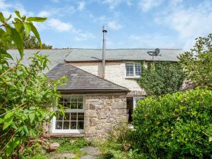 a stone house with a window and bushes at Mayrose Cottage in Lanteglos