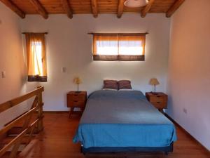 um quarto com uma cama azul e 2 janelas em Cabaña La Yumba em Capilla del Monte