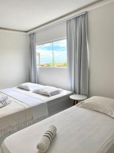 2 bedden in een witte kamer met een raam bij Villa Jundu in São Miguel do Gostoso