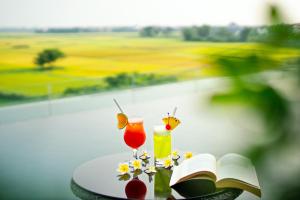a table with a book and two cocktails and flowers at Lasenta Boutique Hotel Hoian in Hoi An