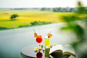 a table with a book and two cocktails and flowers at Lasenta Boutique Hotel Hoian in Hoi An