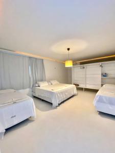 drie bedden in een kamer met witte muren en witte vloeren bij Villa Jundu in São Miguel do Gostoso