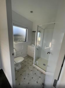 a white bathroom with a toilet and a shower at Kapanga Escape in Coromandel Town