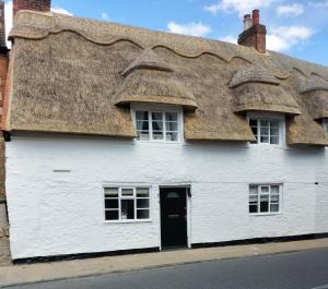 a white building with a thatched roof at Grade Two Listed Cosy Cottage 