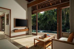 a living room with a tv and a large window at Cicada Luxury Resort - Ubud in Tegalalang