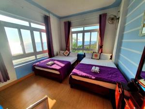 a bedroom with two beds with purple sheets and windows at Thanh Tran Guesthouse Lý Sơn in Ly Son