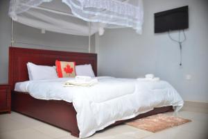 Schlafzimmer mit einem Bett mit weißer Bettwäsche und einem TV in der Unterkunft Elgon Palace Hotel - Mbale in Mbale