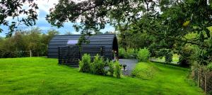 a black building in the middle of a grass field at Odli Glamping - Deri in Welshpool
