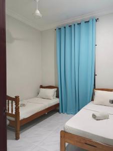 two beds in a room with blue curtains at Inara Homestay Besut in Jertih