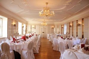 een feestzaal met witte tafels en stoelen en een kroonluchter bij Schlosshotel Neufahrn in Neufahrn in Niederbayern