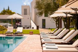 a row of lounge chairs and umbrellas next to a pool at Santiago Hotel in Santiago do Cacém