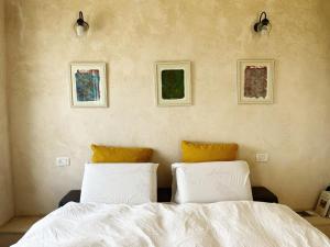 a bedroom with a white bed and three pictures on the wall at Benichuta in Mitzpe Hila