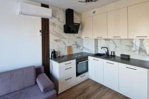 a kitchen with white cabinets and a couch in a room at Comfy apartment near the sea in G ski in Gąski