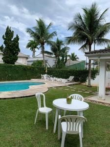 een tafel en stoelen in het gras naast een zwembad bij Guarujá/Acapulco Cond alto padrão in Guarujá