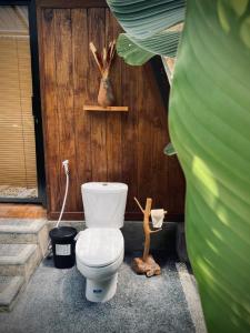 a bathroom with a toilet in front of a wooden wall at Kabinji Bali in Tampaksiring