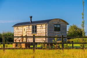 a wooden house with a black roof behind a fence at Monkwood Shepherds Hut - Ockeridge Rural Retreats in Worcester