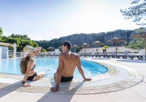 un hombre y una mujer sentados junto a una piscina en Domaine Lou Capitelle & Spa en Vogüé