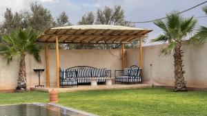 a gazebo with a bench and two palm trees at Villa Nisrine Your Private Oasis With Pool and No Overlooking in Marrakech