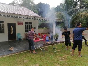 a group of men standing around a grill in a yard at Homestay D'reendang in Yan