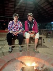 dwie kobiety siedzące na ławce przed ogniem w obiekcie Edgestay w mieście Mudigere