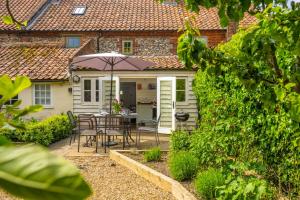 ein kleines Cottage mit einem Tisch, Stühlen und einem Sonnenschirm in der Unterkunft Jasmine Cottage in South Creake