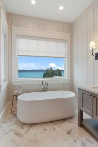 La salle de bains est pourvue d'une grande baignoire blanche et d'une fenêtre. dans l'établissement Torch Lake Grand, à Kewadin