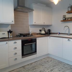 a kitchen with white cabinets and a stove top oven at Hideaway Cottage - Private ensuite room - 4 minutes to the sea! in Sandgate