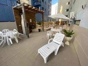 eine Gruppe weißer Stühle und Tische auf einer Terrasse in der Unterkunft Confortável Apto com Manobrista Wi-fi - Tv Smart - piscina - Apto 703 in Maceió