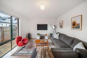 un soggiorno con divano grigio e sedia rossa di Poppy on the Lane - WiFi CBD a Thebarton