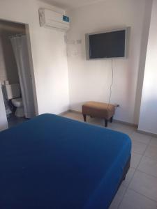 1 dormitorio con 1 cama azul, 1 silla y TV en Hotel CBA en Córdoba